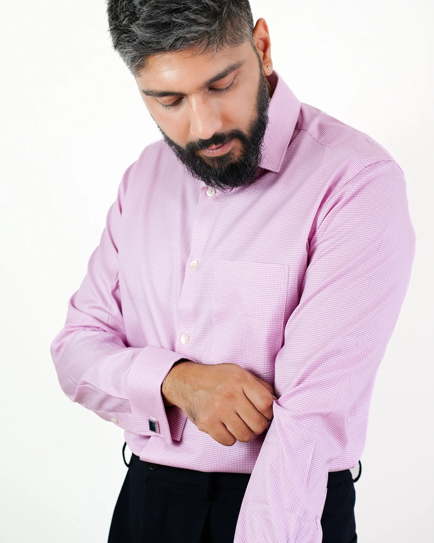 Man in a pink micro check shirt adjusting his cuff, standing against a white background.