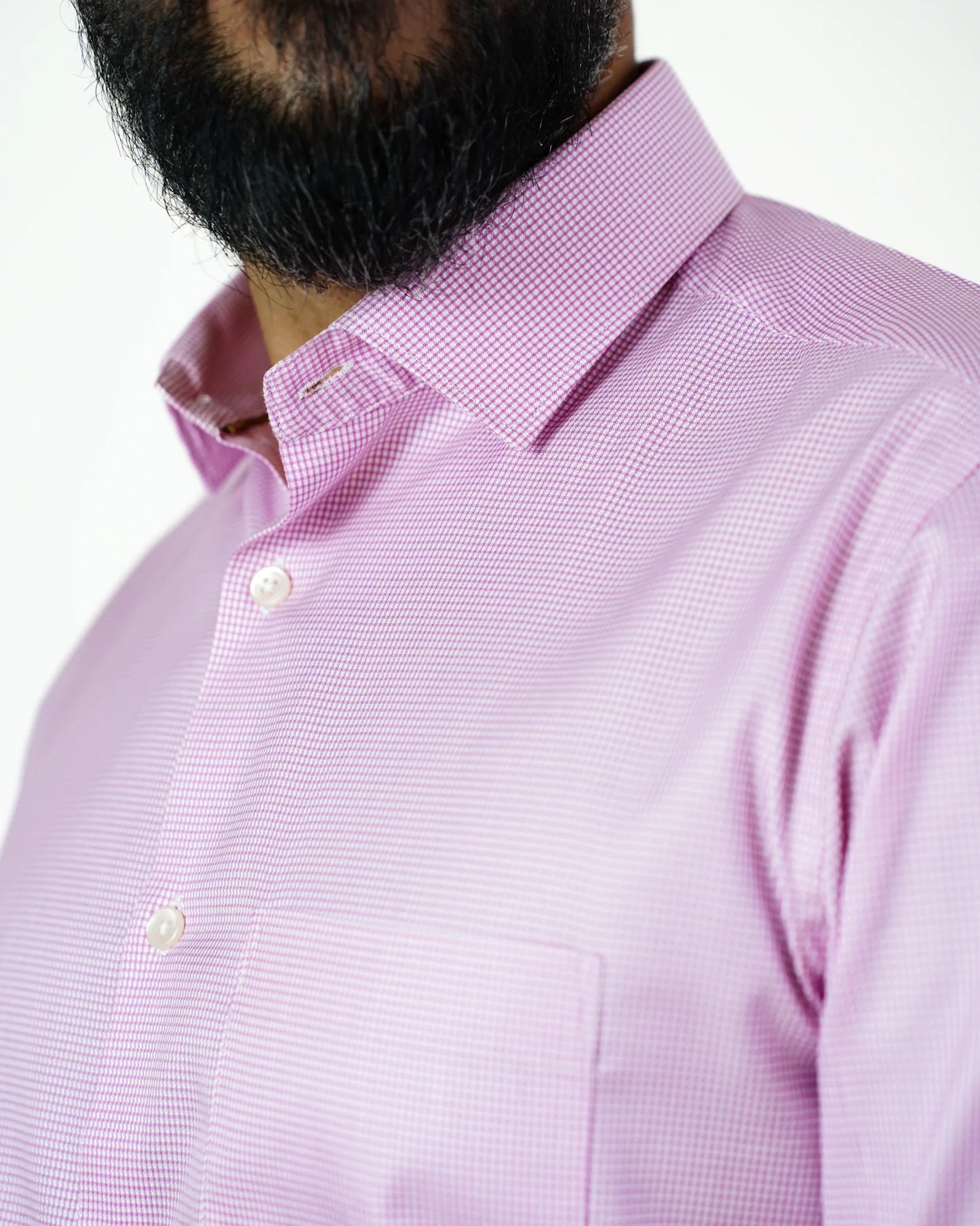 A person wearing a pink micro check shirt with a beard visible, against a plain background.