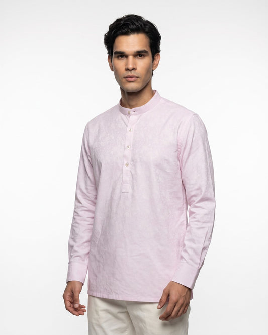 A man wearing a light pink long-sleeve kurta with a mandarin collar and a three-button placket, paired with off-white trousers, photographed against a plain white studio background.